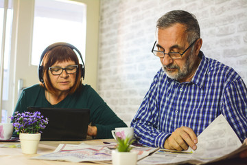 Family, technology, drinks and people concept - happy senior couple with tablet pc computer drinks coffee at home. Toned picture. Headphones.