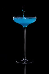 Colorful cocktail with splashes in a glass on a high thin leg is isolated on black with reflection.