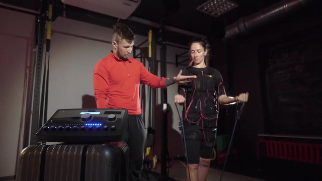 EMS electro stimulation sports equipment in gym. Trainer and woman doing exercises