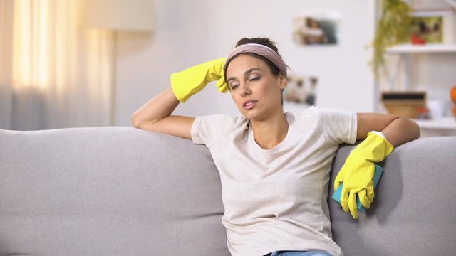 Exhausted woman in gloves sitting on sofa, relaxing after house cleaning work