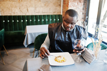 African man in black traditional clothes sitting at restaurant and eat pasta and drink wine.