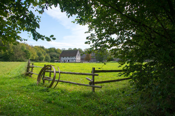 Blick über eine grüne Wiese zu einem alten Bauernhaus