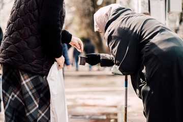Photo of passerby givining alms for old hungry homeless female beggar on street