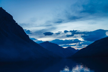 Amazing blue silhouettes of mountains on dusk. Dawn sky reflected in mountain lake. Wonderful atmospheric highland landscape. Beautiful ripples on lake water with twilight bright. Scenic mountainscape