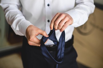 People, business,fashion and clothing concept - close up of man in shirt dressing up and adjusting tie on neck at home.