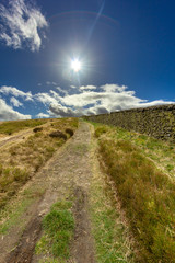 A view of a trail path along stone wall under a majestic blue sky, shanny sun and white clouds