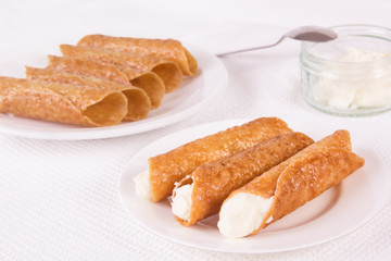 Cream filled brandy snaps and unfilled snaps and a pot with cream