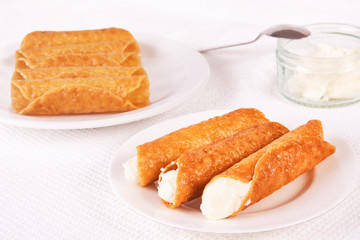 Cream filled brandy snaps served on a plate. Unfilled snaps and a pot with cream in the background