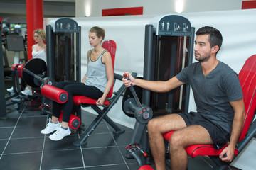 Naklejka premium people flexing muscles on leg press machine in gym