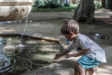 A tender toddler plays with water from a fountain in a park