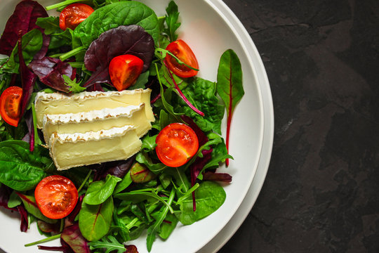 salad, leaves salad mix, tomato and cheese in a white plate (mix micro greens, juicy snack). food background - top view