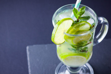 Mojito with ice on black background. Mojito cocktail with lime and fresh mint on slate board. Summer refreshing cocktail with citrus and ice on dark background