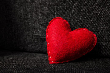 Red valentines day heart made from wool on dark fabric background. Concept of love 
