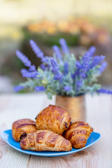 Obraz na płótnie Canvas Croissants and buns with chocolate on a blue plate. Cooking and dessert. Bouquet of lavender flowers. Soft focus. Blurry background. Copy space.