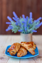 French croissants and buns with raisins on a wooden table. Cooking and dessert. Bouquet of lavender flowers. Soft focus. Blurry background. Copy space.