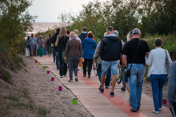 Romantic bonfire night at seaside during sunset. People gathering together to celebrate Night of ancient lights. Walking on wooden pathway on seaside on lit candle path during sunset