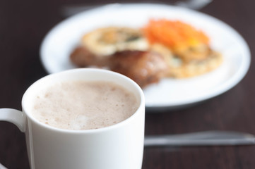 Morning coffee with milk and froth in a white cup on a blurred background of a perfect breakfast on a white plate on a wooden table as a perfect start to the day.