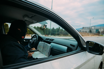 Bank robbers with their masks on pointing at the map prepared for robbing the bank,sitting in the car and waiting for the right time to rob.