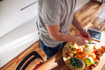 Vegan man in his 20's has a morning preparation of a smoothie while looking at a recipe on his tablet.