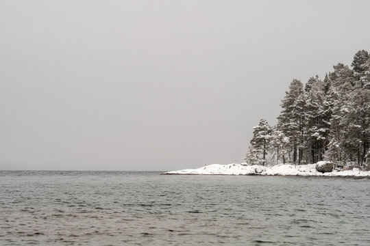 landscape image of lake with trees with snow and fog in the background