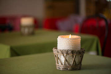 Lit up candle in wicker wooden basket standing on table in restaurant or dining room on green, natural linen tablecloth. Romantic atmosphere for couples, time for dinner. Cosy home, clean sheets

