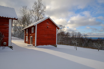 sun shining on a red cottage in a winter landscape