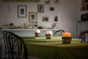 Lit up candle in wicker wooden basket standing on table in restaurant or dining room on green, natural linen tablecloth. Romantic atmosphere for couples, time for dinner. Cosy home, clean sheets
