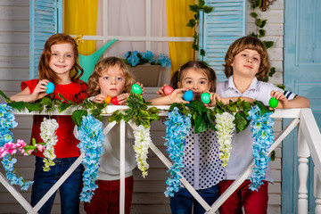 Four beautiful children, two boys and two girls stand on a wooden threshold with Easter eggs in...