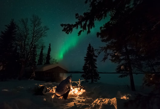 Person sits by campfire under northern lights
