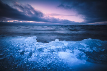 ice that has washed up on beach clouds and sunset in background