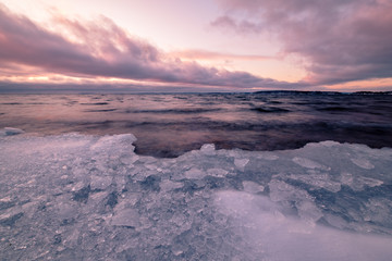 Naklejka na ściany i meble ice that has washed up on beach clouds and sunset in background