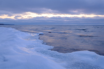 ice and snow on a beach in the foreground, clouds and a streak of light in the background