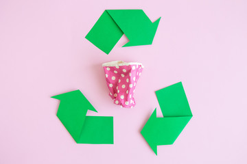 Flat lay of paper coffee cup and recycle symbol on rose.