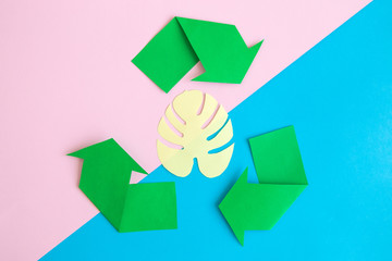 Recycling sign and origami tropical palm leaf on colorful background.