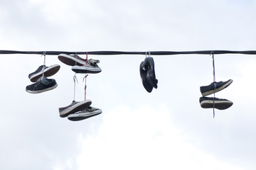 Old sneakers and high heel shoes hanging on electrical wire on overcast background.  