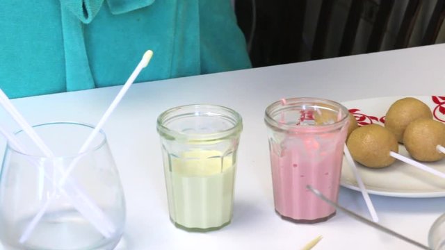 Biscuit balls with sticked chopsticks for making pop cakes lie on a plate. Near the table are glasses with icing.