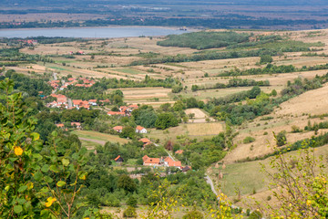 Naklejka premium Beautiful, fresh morning in medieval mountain village with church in the middle, next to meadow. Farming in countryside between hills and dark green forest. Bright sunlight and fog all around city 