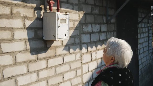 Old woman in glasses looking at gas meter reading