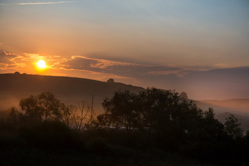 Beautiful morning in mountains. Thick fog covering the hills. Sunlight and rays trying to break through haze and trees