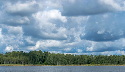 Landscape with river and forest on horizon. Cumulus clouds in sky. Latvian nature. Summer day.