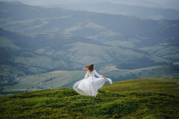 woman in a wedding dress runs across the field toward the mountains