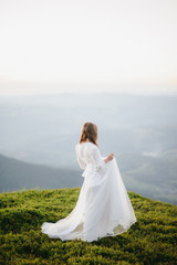 Fototapeta na wymiar woman in a wedding dress runs across the field toward the mountains