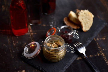 liver pate with nuts and croutons in a glass jar on a dark background