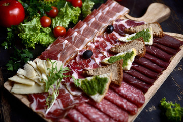 slicing of sausage and meat with croutons and olives on a wooden board