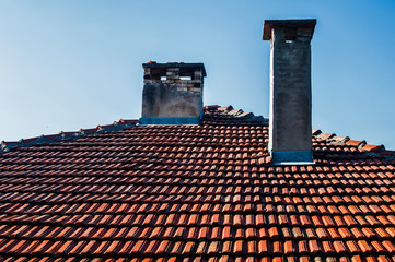 Fototapeta premium Tiled house roof with two weathered chimneys on blue sky background