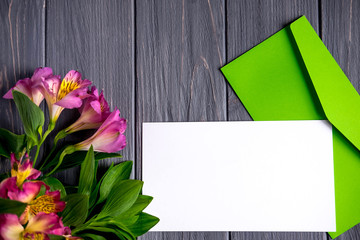 Obraz premium Mock up blank paper on dark wooden background with natural flowers of pink color. Blank, frame for text. Greeting card with flower. Aalstroemeria on wooden background. Flat lay, top view.