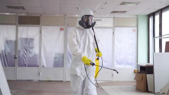 Exterminator in overalls and a protective mask sprays pesticide with a sprayer