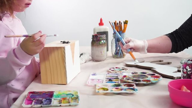 Time lapse. Little girl painting a white unicorn with acrylic paint on a wooden box.