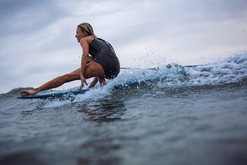 Young woman in swimsuit surfing wave on longboard