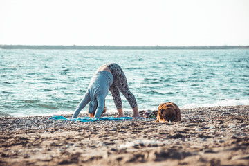 young woman doing yoga and stretching on the beach with her dog